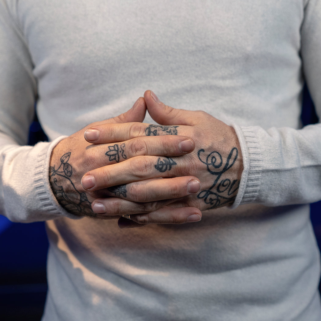 Close up on the hands of a man in an event location wearing a white, seamless merino & cashmere pullover.