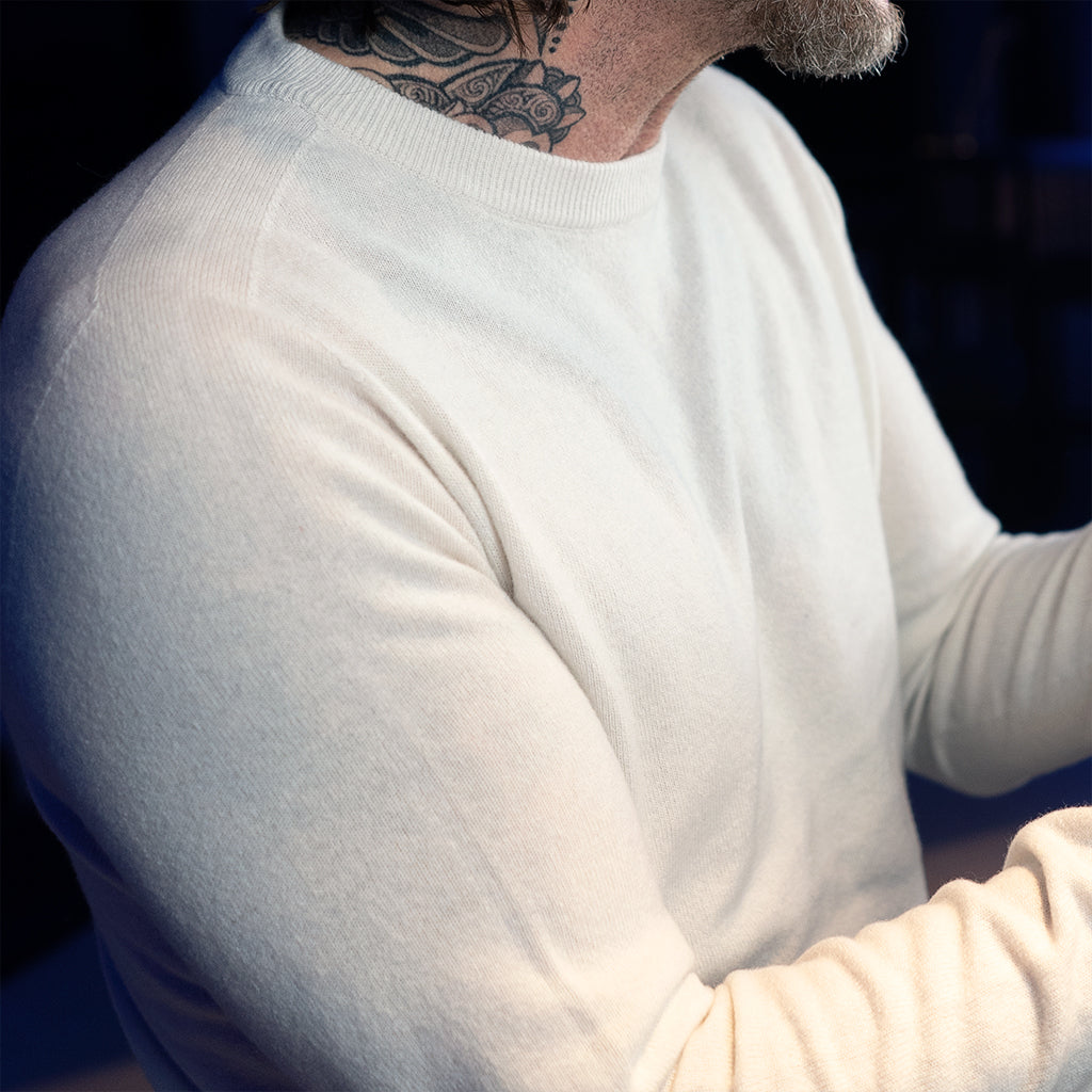 Close up on the chest of a man in an event location wearing a white, seamless merino & cashmere pullover.