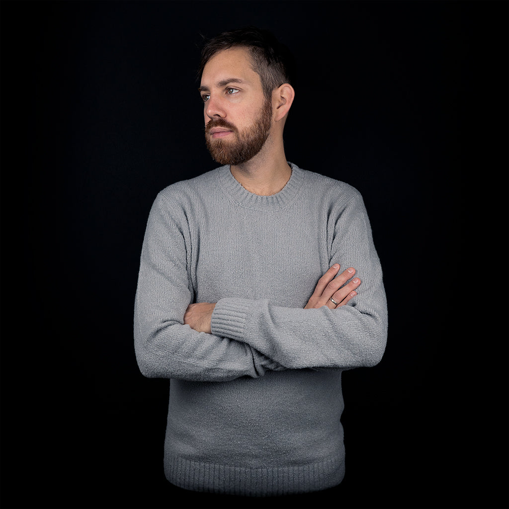 Man wearing a grey organic cotton pullover in front of black background.