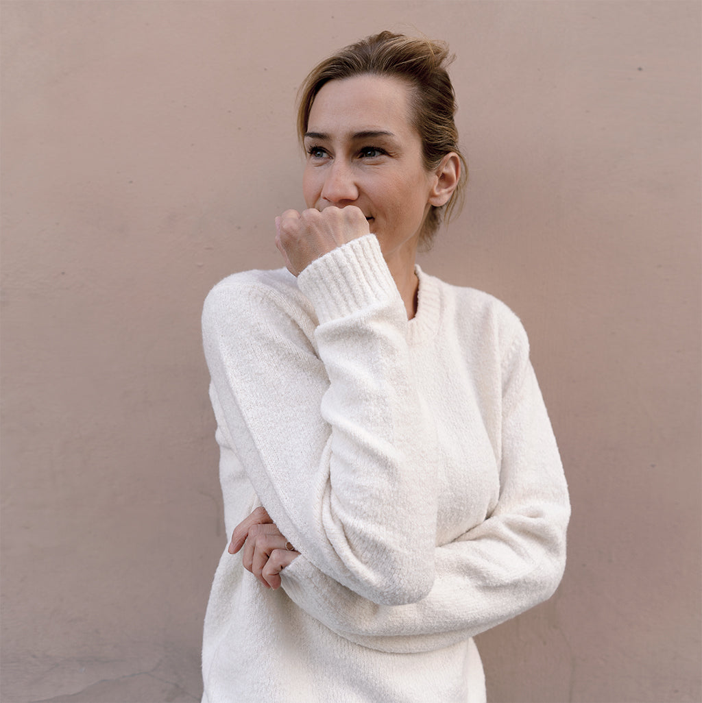 Woman wearing white organic cotton pullover in front of beige wall.